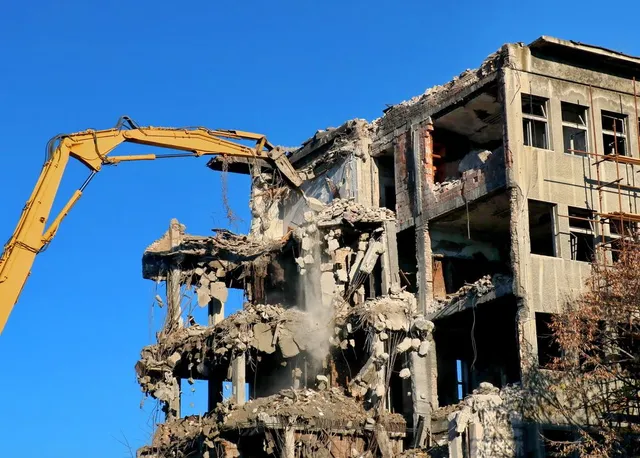 Crawler excavator dropping concrete slab on multi-story building deconstruction site in Delhi